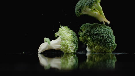 Viele-Grüne-Frische-Brokkoli-Fallen-Auf-Ein-Glas-Mit-Spritzern-Und-Wassertropfen-In-Zeitlupe-Auf-Dunklem-Hintergrund.-Zutaten-Für-Salat,-Gesunde-Ernährung.